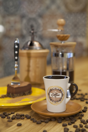 A cup of coffee and a piece of cake placed on a table with a coffee maker in the background.の写真素材