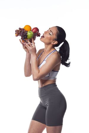 Sexy brunette woman in fitness suit eating fruits. Studio shoot isolated on white background.の写真素材