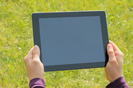 Woman hands holding tablet PC on green grass backgroundの写真素材