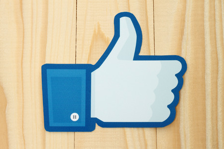 KIEV, UKRAINE - JANUARY 10, 2015: Facebook thumbs up sign printed on paper and placed on wooden background. Facebook is a well-known social networking service.のeditorial素材