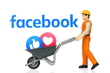 Kiev, Ukraine - November 27, 2019: Toy man holds wheelbarrow with Facebook Like and Love reactions. Facebook is a well-known social networking serviceのeditorial素材