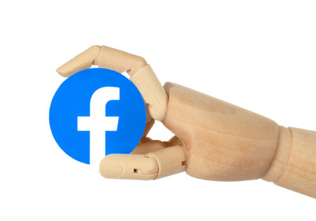 Kiev, Ukraine - May 03, 2022: Wooden hand holds round Facebook paper icon, on white background. Facebook is a well-known social networking serviceのeditorial素材