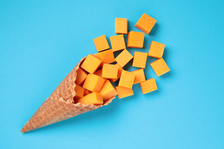 Waffle Cone with Yellow Cheese Cubes on blue background close-up