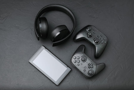 Black devices: gamepads, headset and tablet pc. Gaming concept on black background close-up