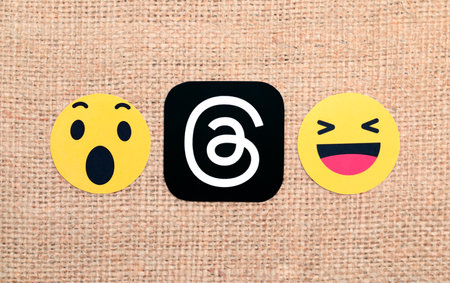 Threads mobile app icon with Wow and Haha Facebook reactions on a sackcloth textile background close-up. Unexpected start Threads service. Meta Officially Launches Threads social media platformのeditorial素材