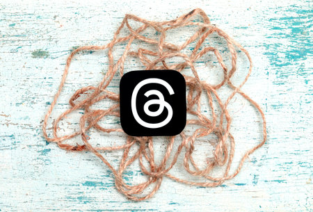 Threads mobile app icon with sackcloth threads on an old painted wood background close-up. Threads service abstract concept. Meta Officially Launches Threads social media platformのeditorial素材
