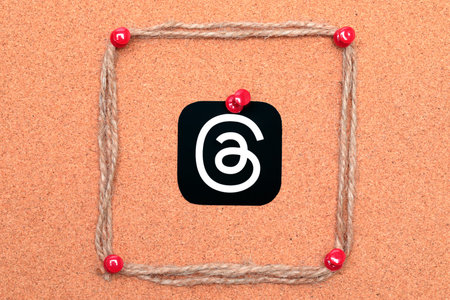 Threads mobile app icon pinned on a cork tree background with pinned sackcloth threads close-up....