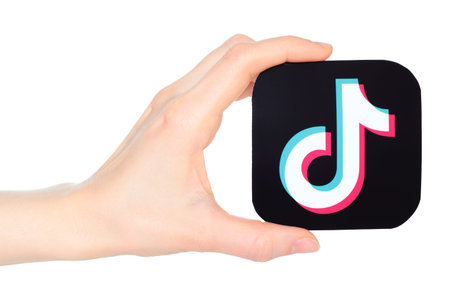Hand holds paper TikTok mobile app icon, on a transparent background. TikTok is a short-form video...