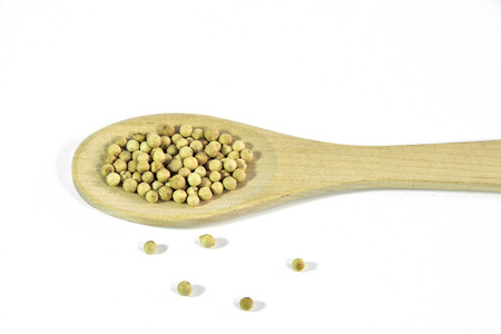 White pepper - fully ripened black peppercorns without shell has a white color, in wooden spoon on a white background isolated. Natural spice and culinary flavor conceptの写真素材