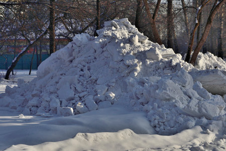 Snowdrift in the city park. Municipal communal services are cleaning snow on roads and alleys of city park. High snowdrift after snowfall or blizzard in snowy siberian winter.の写真素材