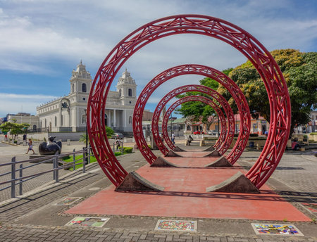 Sculpture of red rings in the middle of a square with a church in the backgroundのeditorial素材