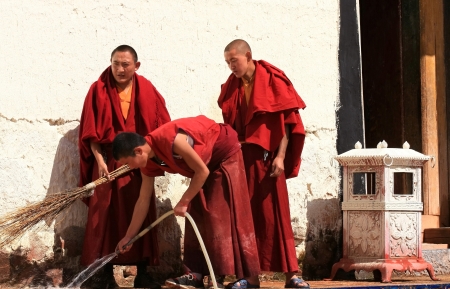 Yunnan, China, October 10, 2011 - Young buddhist monks in red dress with a water hose and a broom scour the entrance to a prayer hall of the Songzanlin Si buddhist monastery in Zhongdian-Shangri La-Gyelthang, Yunnan, China.のeditorial素材