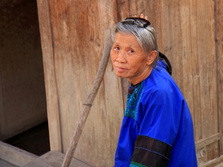 Guizhou, China, October 17, 2011 - Old woman of the Dong people returns home after having worked in a nearby square extending paddy rice on the ground to get it sun dried as to prepare the harvest for wintertime in the village of Rui Li of Rongiang countyのeditorial素材