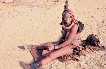EPUPA, KAOKOLAND/NAMIBIA - OCTOBER 16: Young Himba woman scraps an ochre stone to get red dust, then to preparate the paste they smear their bodies with on October 16, 2010 in a seasonal settlement near Epupa, Kunene region, Kaokoland, Namibia.のeditorial素材