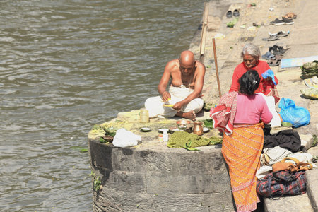DEOPATAN, KATHMANDU, NEPAL - OCTOBER 5  Bhatta priest attends two faithful women and receives their offerings-left bank Bagmati river on October 5, 2012 in the Pashupatinath temple-Deopatan-Kathmandu-Nepal  のeditorial素材