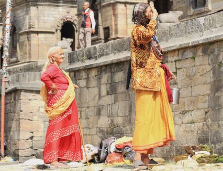 DEOPATAN, KATHMANDU, NEPAL - OCTOBER 5  Yellow dressed tall sadhu greets the faithfuls who expect for him to attend them and waits for their offerings on the Bagmati river left bank on October 5, 2012 in Pashupatinath temple-Deopatan-Kathmandu-Nepal のeditorial素材