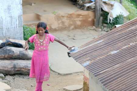 DHAMPUS, NEPAL - OCTOBER 8  Small nepalese young woman cuts onions in a pot over the tin roof of a shed in her house s courtyard on October 8, 2012 in Dhampus village on the Annapurnas Tour trekking route through the foothills of the Himalayas-Kaski distrのeditorial素材