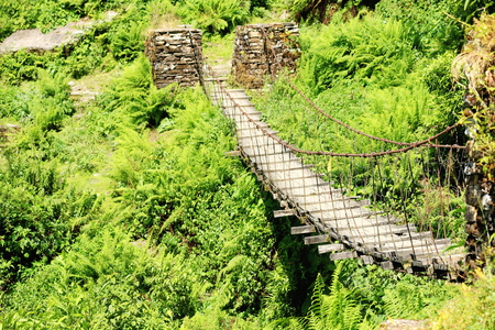 Steel cable and wooden floor suspension bridge crossing a mountain brook on the Pitam Deurali-Tolka sector of the Annapurnas Tour trekking route through the foothills of the Himalayasの写真素材