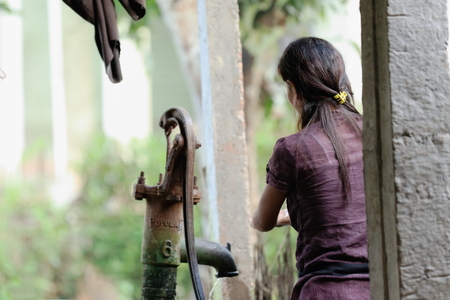 PATIHANI, NEPAL - OCTOBER 13: Young woman of the tharu people washes some clothes-old hand water pump in a bamboo and reef shed on October 13, 2012 in Patihani-Chitwan distr.-Narayani zone-Nepal.のeditorial素材