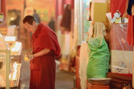 DREPUNG, TIBET, CHINA - OCTOBER 19: Tibetan buddhist monk lights candles in the Sutra Hall of the Coqen Hall on October 19, 2012 in Drepung-Rice Heap monastery. Lhasa pref.-Tibet A.R.-China.のeditorial素材