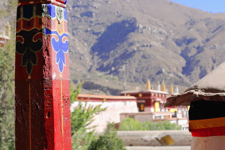 Red painted wooden pillars with colorist drawings-view over the roofs to the mountain. Drepung-Rice Heap monastery of Gelugpa-Yellow Hat order at the foot of mt.Ghephel. Lhasa pref.-Tibet A.R.-China.の写真素材