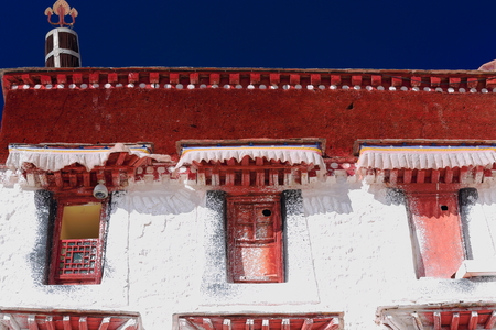 Red windows on whitewashed wallwooden dhvaja on rooftop. With the Potala palace Potrang Karpo and MarpoRed and White palaces to the E.and W.at 3700 ms.high on Marpo RiRed Hill 300 ms.over the valley. LhasaTibet.のeditorial素材