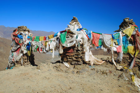 Five colored buddhist prayer flags hanging from cairnsstacked stones seemingly of slate half way up...