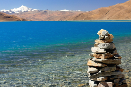 Cairnstone stack on the shore of the 638 km2130 km.E'W70 km.N'S wide250 long bank4441 ms.highturquoise colored Yamdrok TsoUpper Pasture lake and 7206 ms.high mt.Nojin Kangsang on the background. Lhoka or Shannan pref.Tibet.のeditorial素材