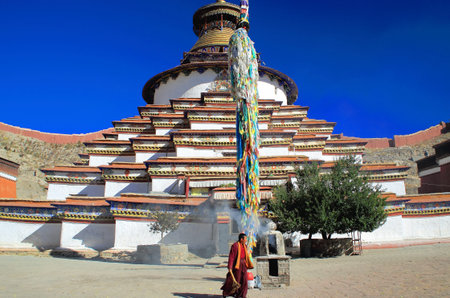 GYANTSE, TIBET, CHINA - OCTOBER 23: Buddhist lama takes care of the fire lit in the yard facing the Kumbum or Tashigomang pagoda of 9 tiers and 76 shrines on October 23, 2012. Gyantse city and county-Shigatse pref.-Tibet.のeditorial素材
