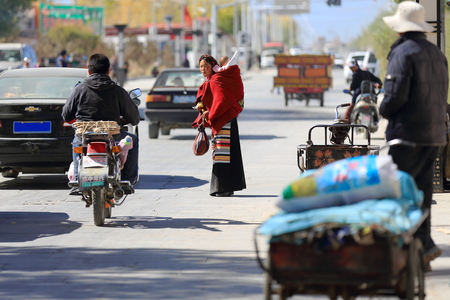 SHIGATSE, TIBET, CHINA-OCTOBER 24: Tibetan woman-child on her back dodges the traffic on a street around the Tashilhunpo-Heap of Glory monast.-seat of Panchen Lama on October 24, 2012. Shigatse-Yarlung Tsangpo and Nyang Chu rivers junction-Tibet.のeditorial素材