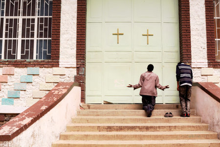 KOMBOLCHA, ETHIOPIA-MARCH 24: Men praying atop a stairway at the closed gate of Bete Gebriel-St.Gabriel orthodox christian church on March 24, 2013. Kombolcha-Debub Wollo zone-Amhara region-Ethiopiaのeditorial素材