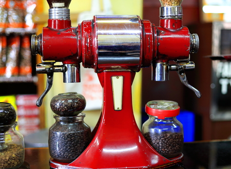 Red painted old italian style vintage coffee grinder along with glass jars containing roasted coffee beans ready to be ground in the Tomoca Coffee Shop of Piazza-downtown area. Addis Ababa-Ethiopia.の写真素材