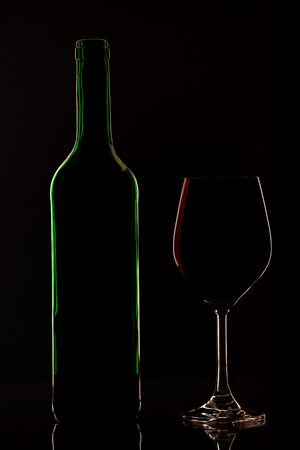 Wine bottle and wineglass in front of dark background. Glowing contoursの写真素材