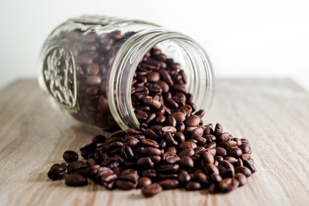Spilled coffee beans from mason jar on wood grain textureの写真素材