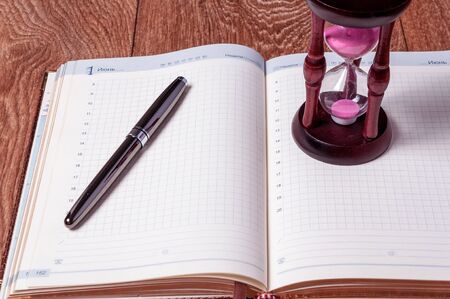 Hourglasses and book on a wooden table.の写真素材