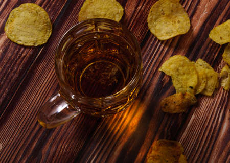 A glass of fresh beer and potato chips on a wooden wooden table.の写真素材