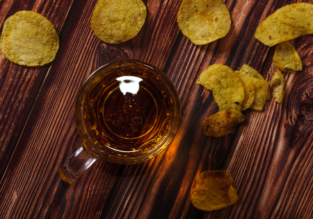 A glass of fresh beer and potato chips on a wooden wooden table.の写真素材