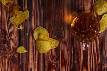 A glass of fresh beer and potato chips on a wooden wooden table.の写真素材