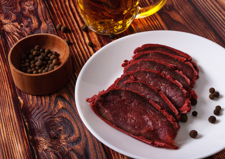 Fresh basturma on a white plate with a glass of beer on a wooden background.の写真素材