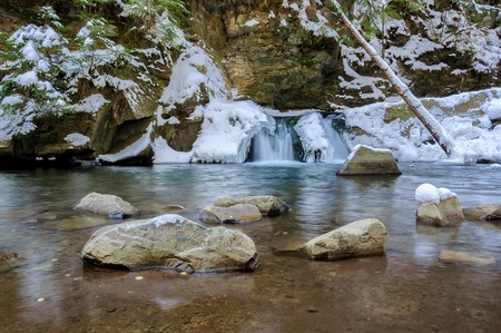 Waterfall in winter. Mountain river and snow on the mountain slopesの写真素材