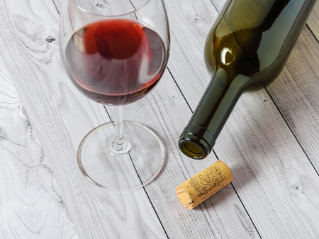 Red wine in a glass and a bottle on a light wooden table.の写真素材