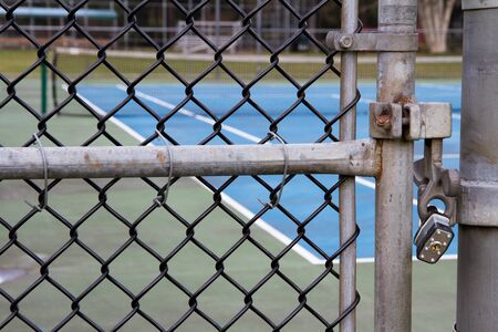 Close up of the padlocked gate of a tennis court with net in background.の写真素材