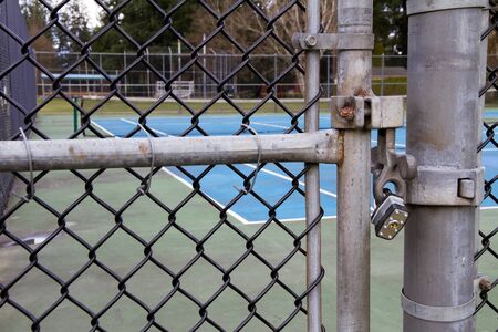 The gate of a tennis court is padlocked shut with tennis net in background.の写真素材