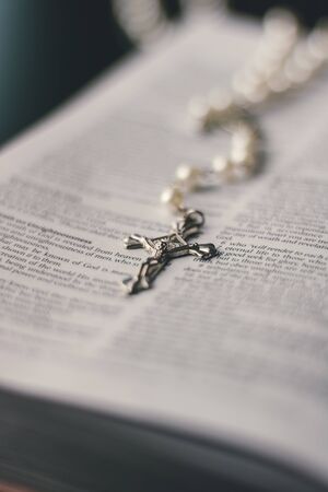 An open bible is placed on a black desktop. On the open page of the bible is a silver and pearl...