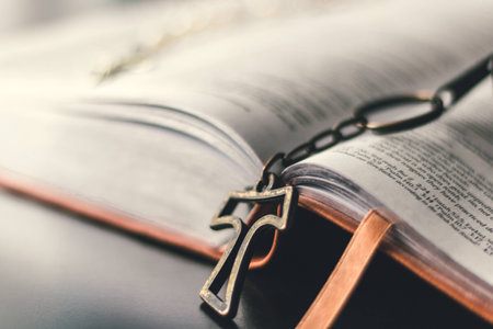 A Tao Cross hangs from the center of the opened bible and slightly rests on the black table top.の写真素材