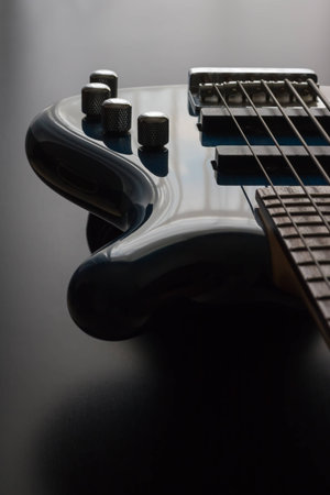 A blue five string bass guitar is strategically positioned in the frame with a black wooden background. This is a darker image which emphasizes the sleek shape of the guitar along with a play on light and shadows.の写真素材