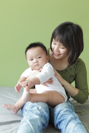 Mother and her baby sit on the bed, model are asian familyの写真素材