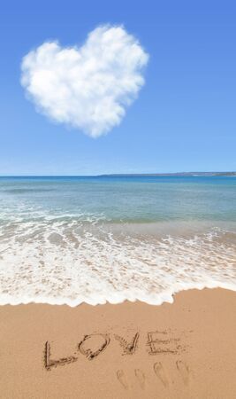 Love text drawn on the beach shore with the blue sky and heart shape cloud in the background. Love Concept.の写真素材