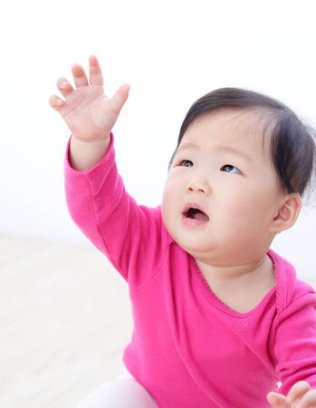 Little girl baby looking up and rise her arm to touch something - isolated on white backgroundの写真素材