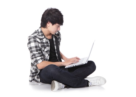 young man sitting on the floor cross-legged with laptop in full length isolated on white background, asian modelの写真素材
